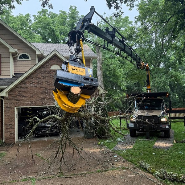 Grapple saw truck lifting an uprooted tree from a residential driveway during tree removal