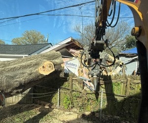 Grapple crane removing fallen tree debris from residential property during emergency response