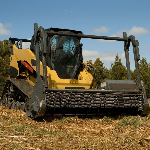 Skid steer with forestry mulcher attachment parked in a cleared field