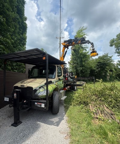 Tree Solutions branded truck with a grapple claw crane loading tree debris in a narrow residential driveway