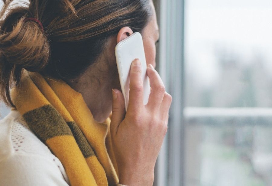 Woman calling a tree care professional by phone while looking out a window.